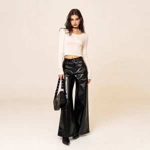 Inquadratura completa di pantaloni in pelle nera lucida a gamba larga con top corto bianco