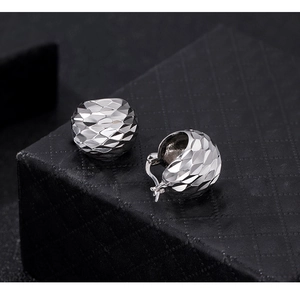 Macro detail of CNC textured silver hoop earrings with shimmering diamond-cut patterns