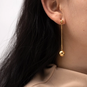 Detail of 18K gold-plated stainless steel earrings with ball pendant worn by a model
