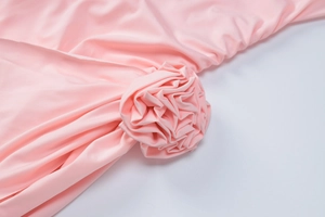 Détail d'une grande rose en tissu 3D sur une robe rose ajustée à manches longues