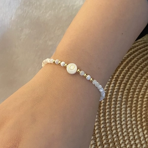 Detailed shot of beaded bracelet with white shell beads and gold letter O pendant