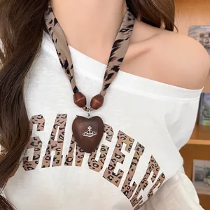 Detail of a heart-shaped wooden pendant with leopard print fabric strap worn by a model