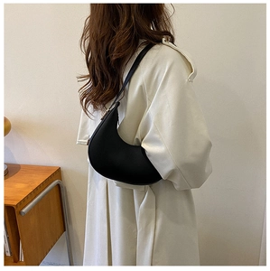 Side view of a chic black crescent underarm bag worn by a model in a cozy home setting