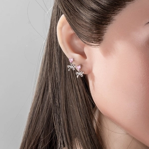 Silver bow stud earrings with pink heart zircon gemstone worn on a model's ear