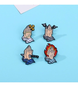 Detail of four enamel pins with praying hands, cross, bat, and flame motifs on blue