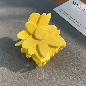 Close-up of a matte yellow flower hair claw clip on a textured background