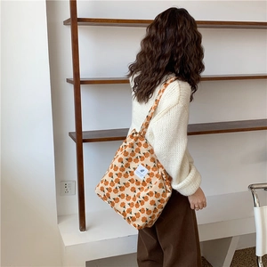 Detalle de bolso tote de pana beige con estampados florales naranjas y un parche blanco