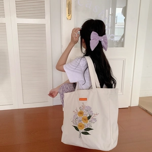 Detail of embroidered floral patterns on a large off-white canvas tote bag