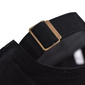 Detail of black cotton baseball cap showing adjustable strap and vintage bronze metal buckle