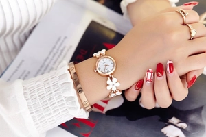 Close-up of white five-leaf flower strap quartz watch on female wrist in gold finish