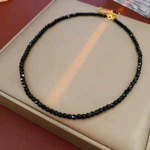 Detail of a black faceted bead necklace with a gold clasp on a minimalist beige tray