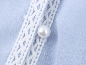 Macro view of light blue fabric with hollow white lace trim and a pearl button detail