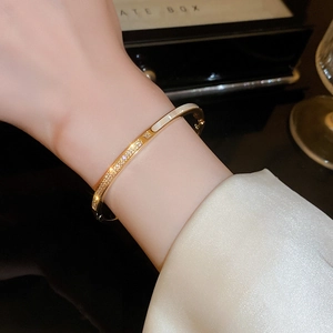 Dettaglio di un bracciale placcato oro con zirconi e smalto bianco indossato al polso
