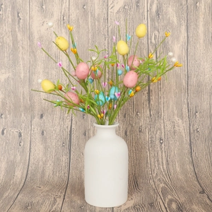 Rami di bacche con uova di Pasqua in vaso di ceramica bianca su sfondo legno