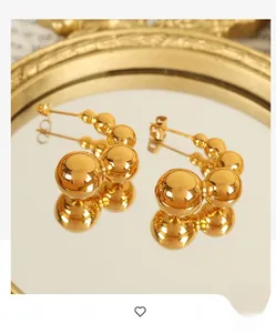Detail shot of golden C-shaped pea earrings with spherical beads on vintage mirror tray
