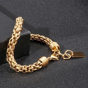 Detail of a gold braided chain bracelet with a circular link and metal tag on black surface