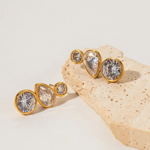 Golden stainless steel earrings featuring white cubic zirconia stones on stone surface