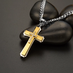 Detail of layered gold and silver cross pendant with small diamonds on black pebbles