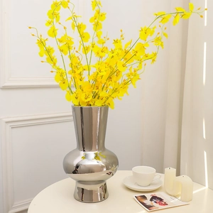 Modern silver ceramic vase with yellow orchid flowers on a white pedestal stand