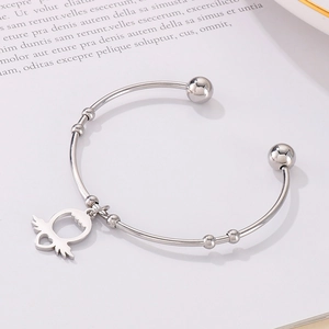 Close-up of silver steel open bangle featuring heart with wings charm on paper background