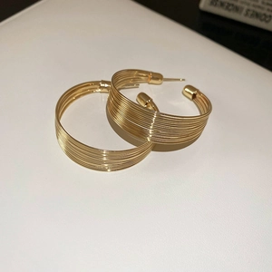 Detail of gold multi-layer thin line hoop earrings on a textured white surface
