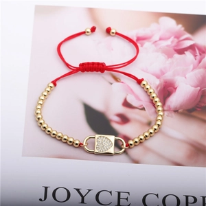 Macro detail of red woven rope bracelet with gold beads and pavé heart charm