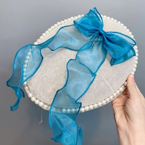 Detail of beige wool beret featuring faux pearl trim and a large royal blue organza bow