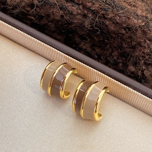 Macro shot of gold C-shaped earrings with brown enamel on a silk texture background