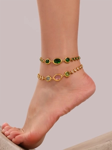 Detail of layered gold anklets featuring oval green crystals and multicolor gemstones