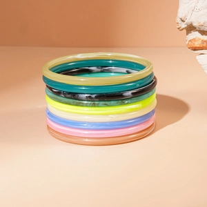 Vertical stack of colorful acrylic resin bangles on a textured white stone background