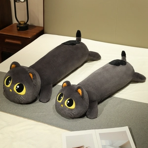 Cute long black cat plush pillow in two sizes on a cozy white bed with a lamp