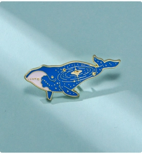 Detail of blue whale enamel pin showing golden starry sky patterns and galaxy details