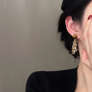 Close-up of elegant gold leaf tassel earrings featuring a round tiger eye gemstone bead