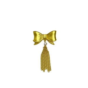 Vintage golden bow brooch with white pearl and metallic fringe on white background