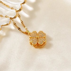 Detailed close-up of a gold clover necklace with shimmering zircon on white silk fabric