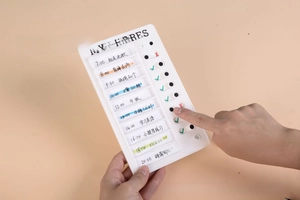 Handheld view of a white plastic daily routine chore chart with green sliding checkmarks