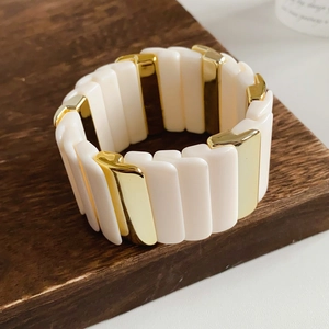 Detail of the golden and white block拼接 wide stretch bracelet on a wooden base