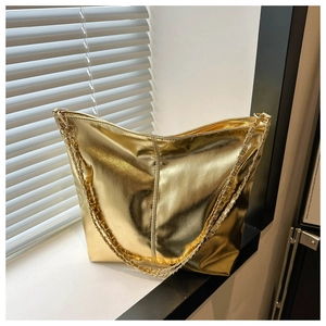 Detail of a shiny gold PU leather tote bag with metallic chain straps in sunlight
