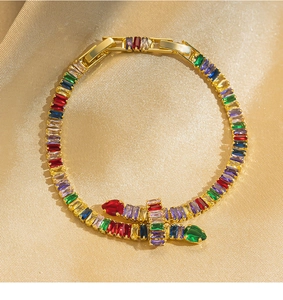 Detail of gold-plated snake bracelet with colorful zircons on golden silk background