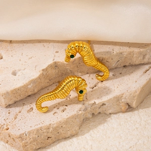 Macro shot of gold seahorse earrings with green zircon eyes on a beige stone surface