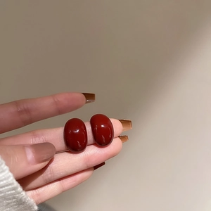 Macro detail of deep red oval earrings with high-gloss finish held in hand