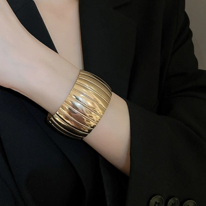 Close-up of a wide gold textured bangle featuring a stylish wavy metal pattern on a model