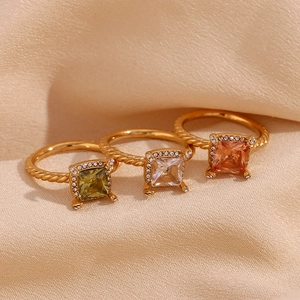 Detailed view of three 18K gold plated rings with colorful square stones on beige fabric
