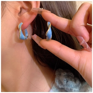 Close-up of blue spiral twist earrings with gold trim worn by a model for elegant style