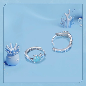 Macro shot of silver sea turtle hoop earrings with blue accents on a coral background