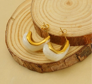 Détail de boucles d'oreilles en acier doré et résine blanche sur support en bois