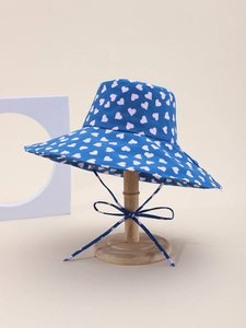Detail of blue sun hat with pink heart pattern and a bow-tied chin strap on a stand