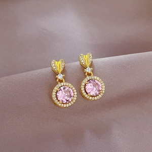 Close-up of gold heart earrings with pink crystals and micro-pave details on velvet