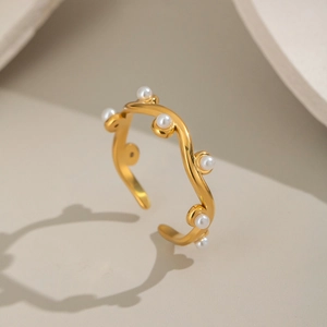 Detailed view of a wave-shaped gold bracelet with six small pearls on neutral background