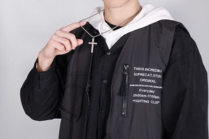 Close-up of a silver polished titanium steel cross pendant worn by a model in streetwear